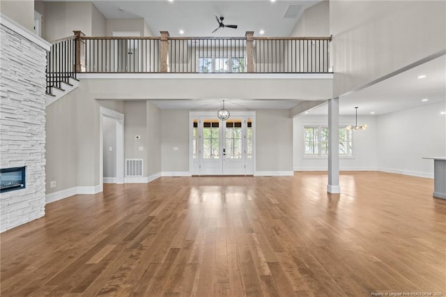 unfurnished living room featuring ceiling fan with notable chandelier, a stone fireplace, wood finished floors, and visible vents