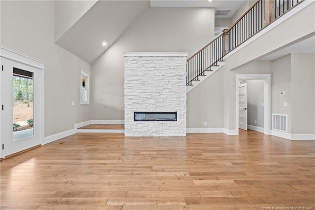 unfurnished living room featuring a towering ceiling, light wood finished floors, a fireplace, and visible vents