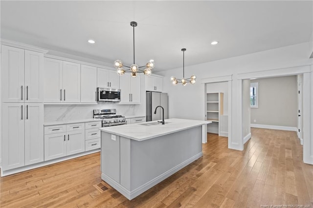 kitchen with a center island with sink, light wood finished floors, stainless steel appliances, white cabinetry, and a sink