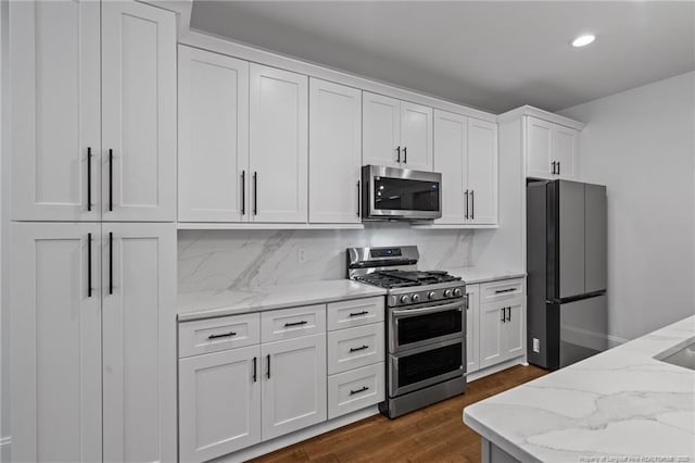 kitchen with white cabinets, decorative backsplash, dark wood-type flooring, light stone countertops, and stainless steel appliances