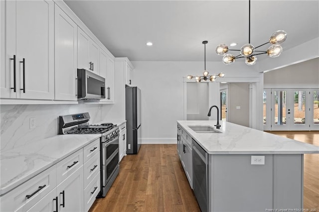 kitchen featuring stainless steel appliances, a kitchen island with sink, a sink, and wood finished floors