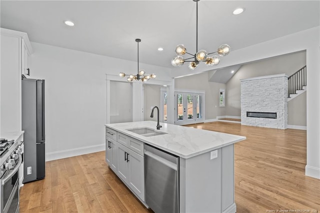 kitchen featuring light wood-style flooring, stainless steel appliances, a fireplace, a sink, and white cabinets