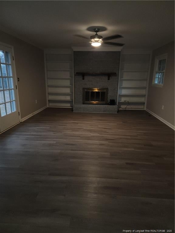 unfurnished living room featuring built in shelves, ceiling fan, a fireplace, and dark hardwood / wood-style floors