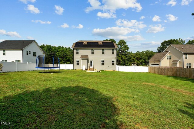 back of property with solar panels, a trampoline, and a lawn