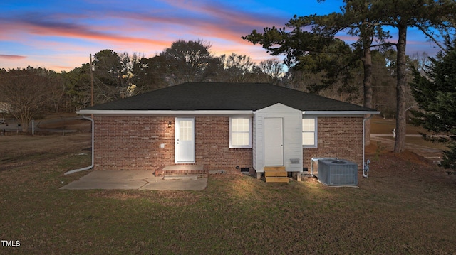 back house at dusk featuring a lawn, a patio area, and central AC