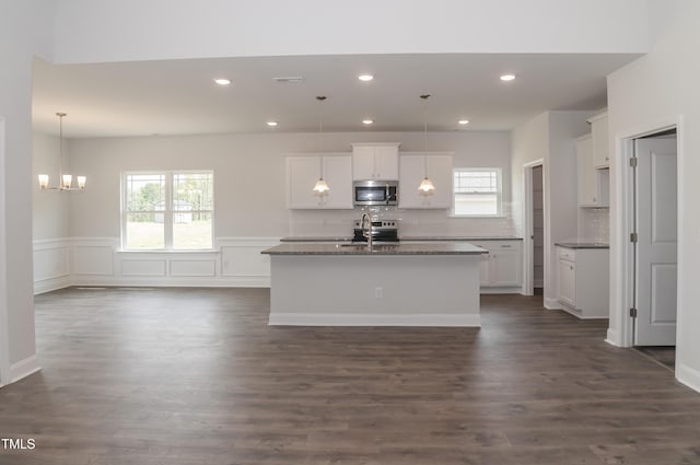 kitchen featuring hanging light fixtures, white cabinets, stainless steel appliances, and a kitchen island with sink