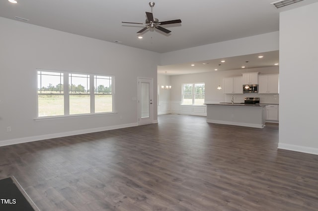 unfurnished living room featuring ceiling fan with notable chandelier and dark hardwood / wood-style floors