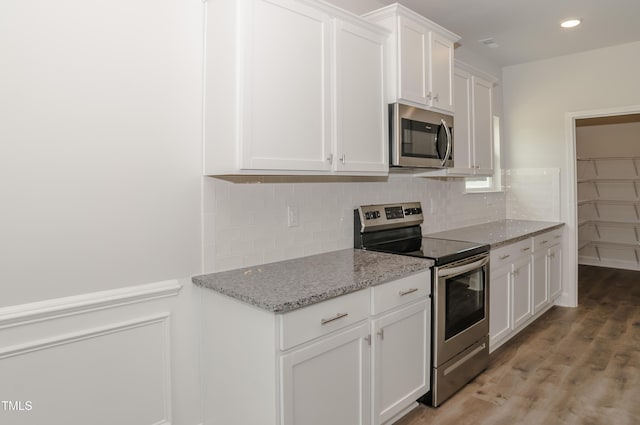 kitchen featuring light stone countertops, white cabinetry, stainless steel appliances, decorative backsplash, and light hardwood / wood-style flooring