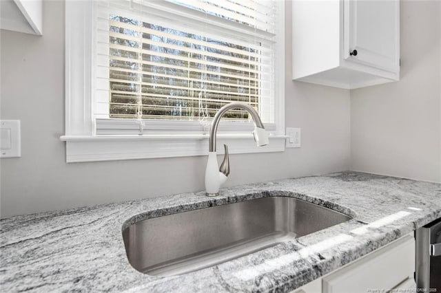 room details featuring white cabinetry, sink, and light stone countertops