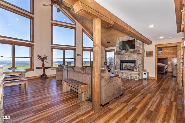 living room with beam ceiling, ceiling fan, a stone fireplace, dark hardwood / wood-style flooring, and a towering ceiling