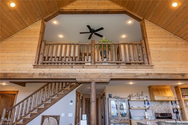 staircase with wooden walls, high vaulted ceiling, wooden ceiling, and ceiling fan