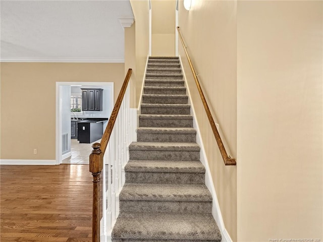 staircase with wood-type flooring and crown molding