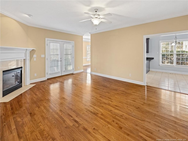 unfurnished living room with ceiling fan with notable chandelier, light hardwood / wood-style floors, ornamental molding, and a tiled fireplace