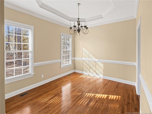 empty room featuring hardwood / wood-style floors, an inviting chandelier, a healthy amount of sunlight, and a tray ceiling