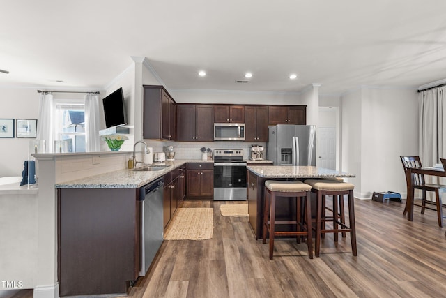 kitchen with hardwood / wood-style floors, a center island, sink, light stone countertops, and stainless steel appliances