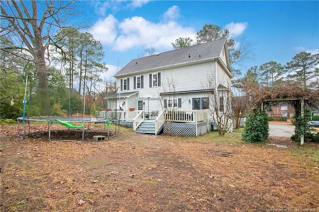 rear view of property with a trampoline and a wooden deck