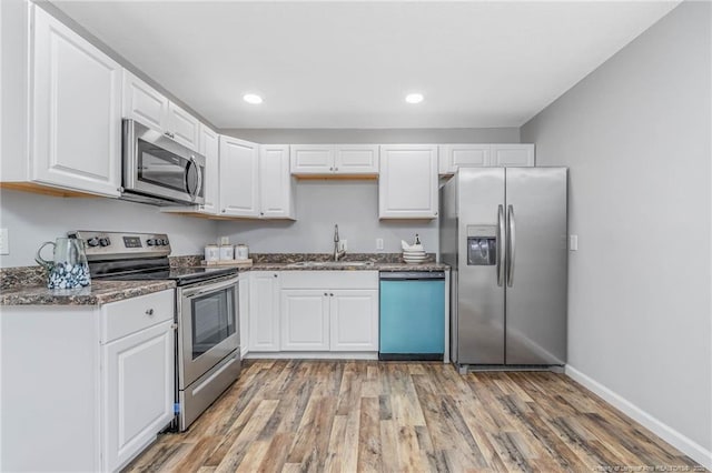 kitchen with sink, appliances with stainless steel finishes, dark stone counters, white cabinets, and light wood-type flooring