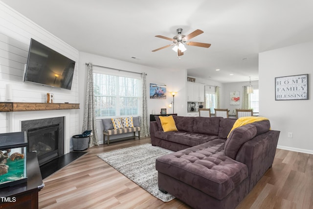 living room with ceiling fan, a large fireplace, and light hardwood / wood-style floors