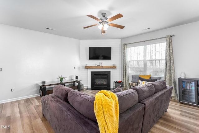 living room with ceiling fan, a large fireplace, and light wood-type flooring