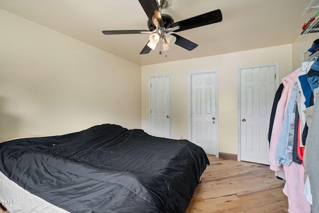 bedroom featuring ceiling fan, light hardwood / wood-style floors, and multiple closets