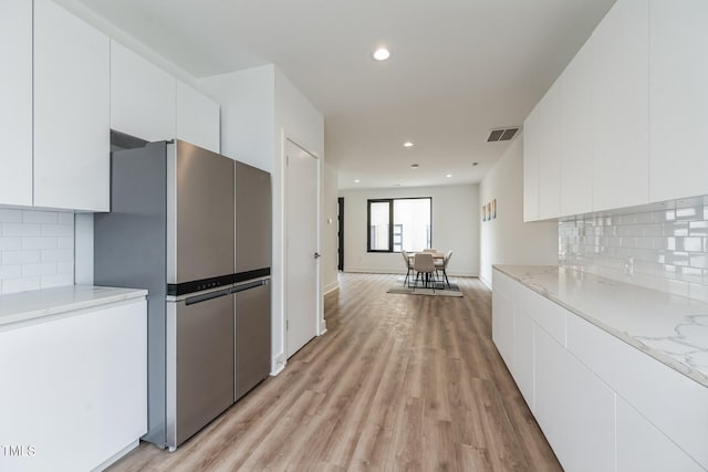 kitchen with backsplash, stainless steel refrigerator, white cabinets, and light hardwood / wood-style floors