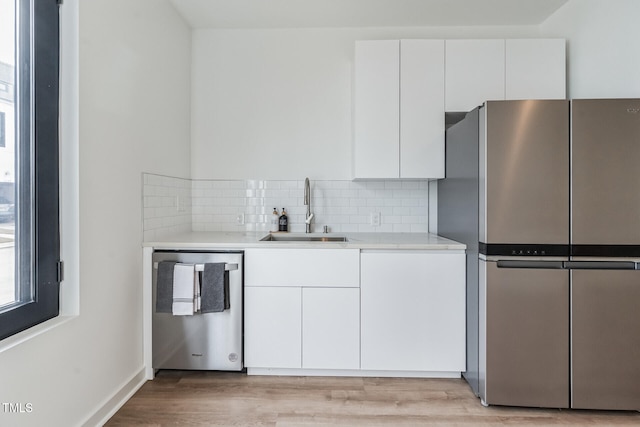 kitchen featuring sink, stainless steel appliances, light hardwood / wood-style floors, decorative backsplash, and white cabinets