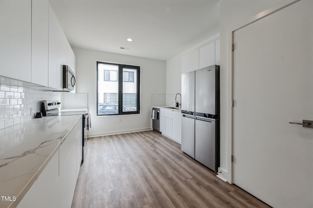 kitchen with white cabinets, sink, light hardwood / wood-style flooring, tasteful backsplash, and stainless steel appliances