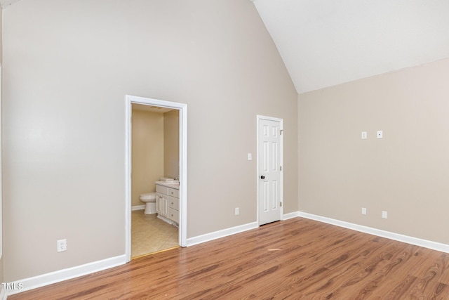 unfurnished bedroom featuring light wood-type flooring, connected bathroom, and high vaulted ceiling