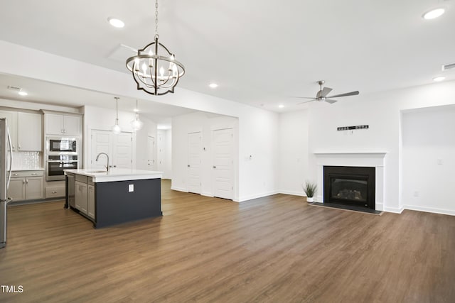 kitchen featuring sink, stainless steel appliances, pendant lighting, gray cabinets, and a kitchen island with sink