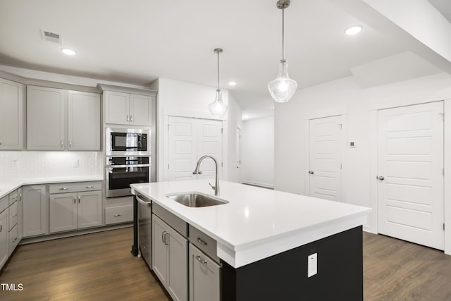 kitchen with sink, hanging light fixtures, a kitchen island with sink, stainless steel appliances, and decorative backsplash