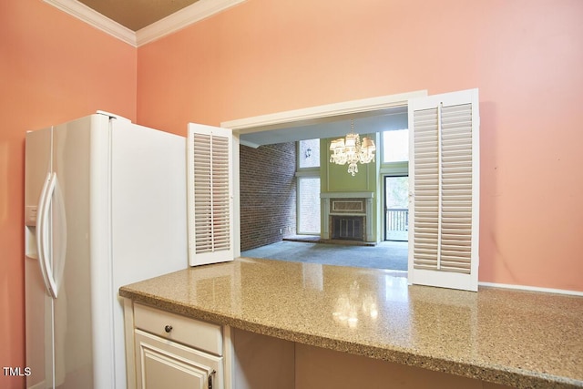 kitchen featuring pendant lighting, crown molding, white fridge with ice dispenser, light stone counters, and a chandelier