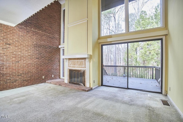 unfurnished living room with carpet flooring, a high ceiling, a brick fireplace, and brick wall