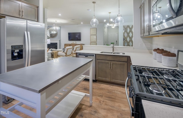 kitchen featuring kitchen peninsula, appliances with stainless steel finishes, sink, hardwood / wood-style flooring, and decorative light fixtures