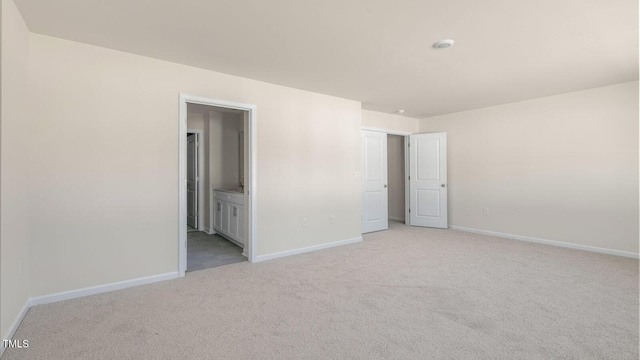 unfurnished bedroom featuring light carpet, baseboards, and ensuite bathroom