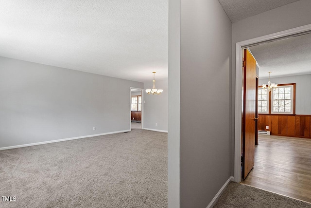 corridor featuring a textured ceiling, baseboard heating, carpet floors, and a notable chandelier