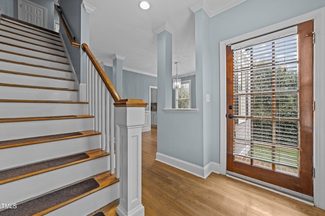 stairs with hardwood / wood-style flooring, a notable chandelier, ornamental molding, and decorative columns