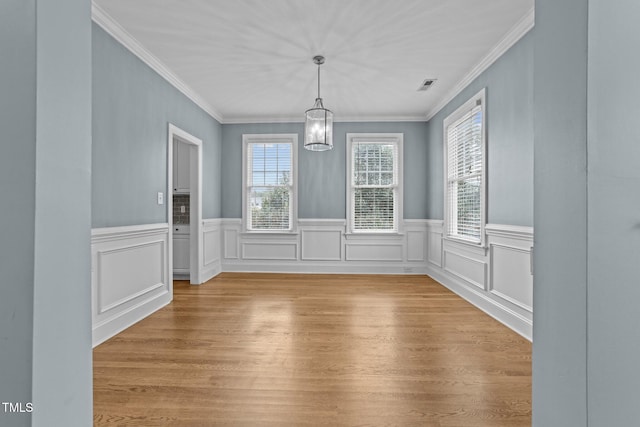 unfurnished dining area featuring a notable chandelier, light wood-type flooring, crown molding, and a wealth of natural light