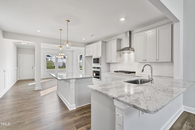 kitchen with a breakfast bar, a sink, appliances with stainless steel finishes, a center island, and wall chimney exhaust hood