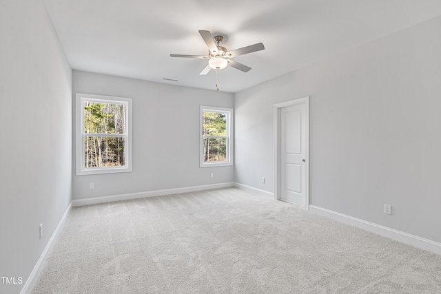 empty room featuring a ceiling fan, light carpet, visible vents, and baseboards