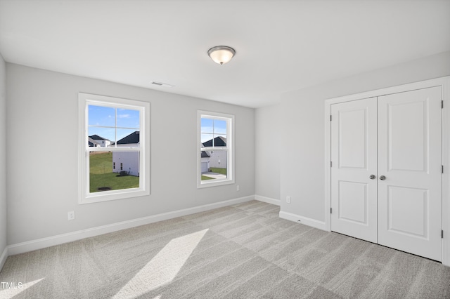 unfurnished bedroom featuring light carpet, a closet, visible vents, and baseboards