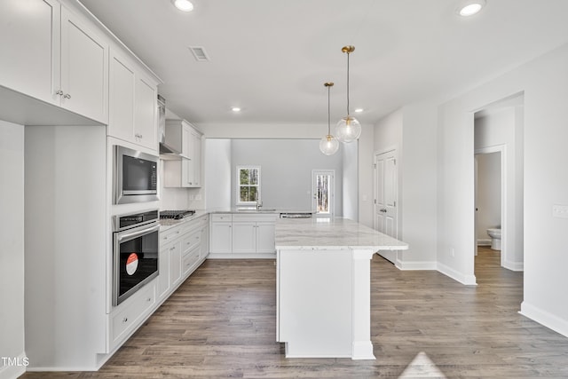 kitchen featuring visible vents, white cabinets, a center island, decorative light fixtures, and stainless steel appliances