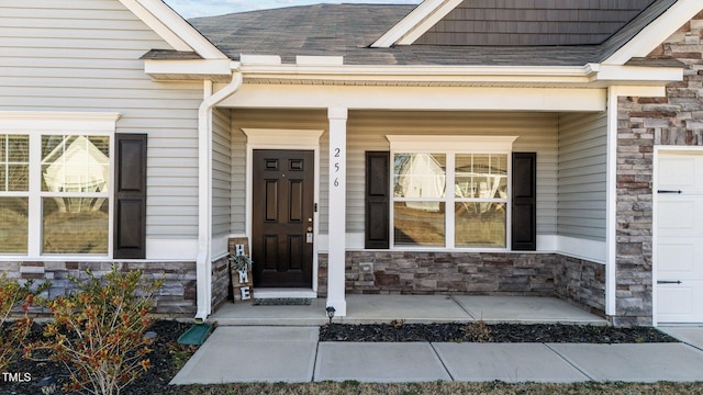 doorway to property with stone siding, a porch, and a shingled roof