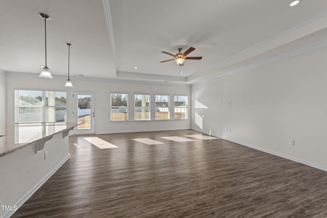 unfurnished living room with a healthy amount of sunlight, dark wood-style floors, a tray ceiling, and crown molding