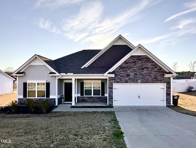 craftsman-style house with a garage, fence, stone siding, driveway, and a front lawn