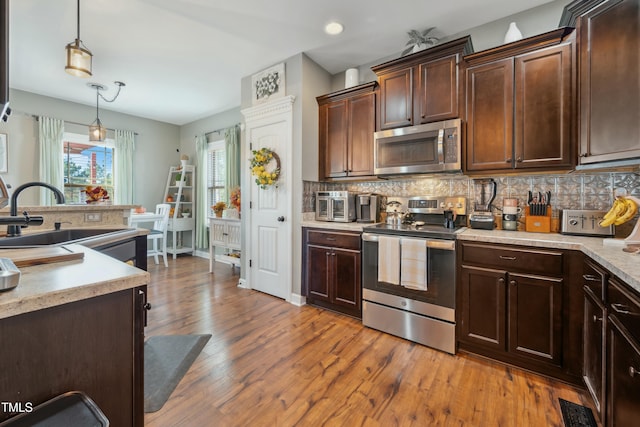 kitchen with decorative light fixtures, stainless steel appliances, dark brown cabinets, and sink