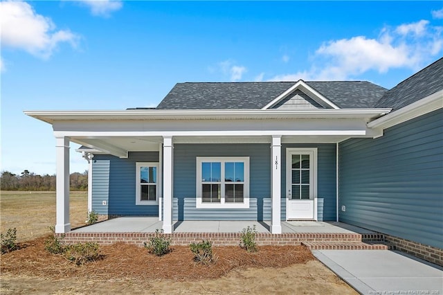 property entrance with covered porch and a shingled roof