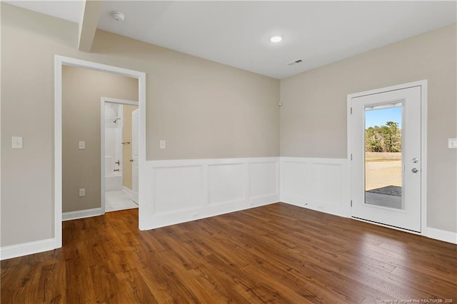 empty room featuring visible vents, wood finished floors, and wainscoting