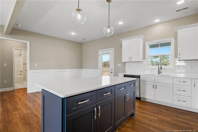 kitchen featuring dark wood-type flooring, light countertops, stainless steel dishwasher, white cabinets, and a sink