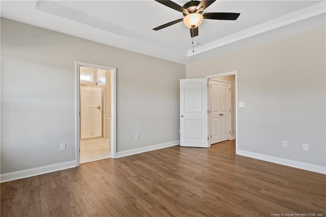 unfurnished bedroom with ensuite bathroom, a tray ceiling, baseboards, and wood finished floors