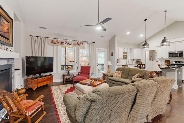 living room with dark hardwood / wood-style floors, a stone fireplace, ceiling fan, and lofted ceiling